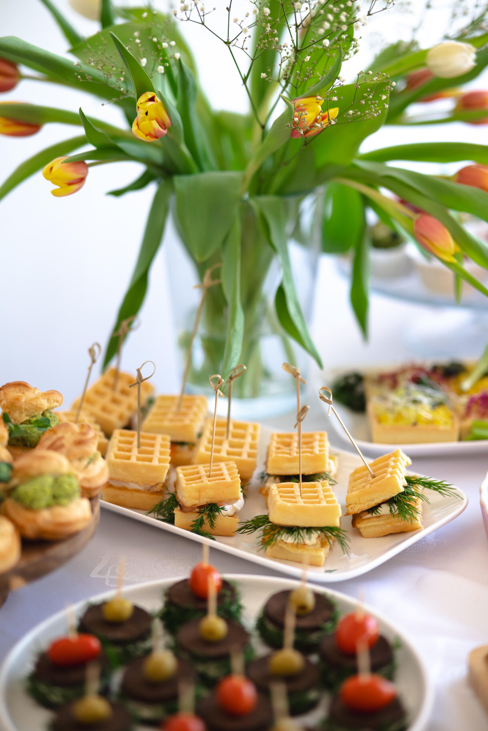 Biały talerz z wytrawnymi goframi w formie kanapek z serkiem, łososiem i koperkiem.